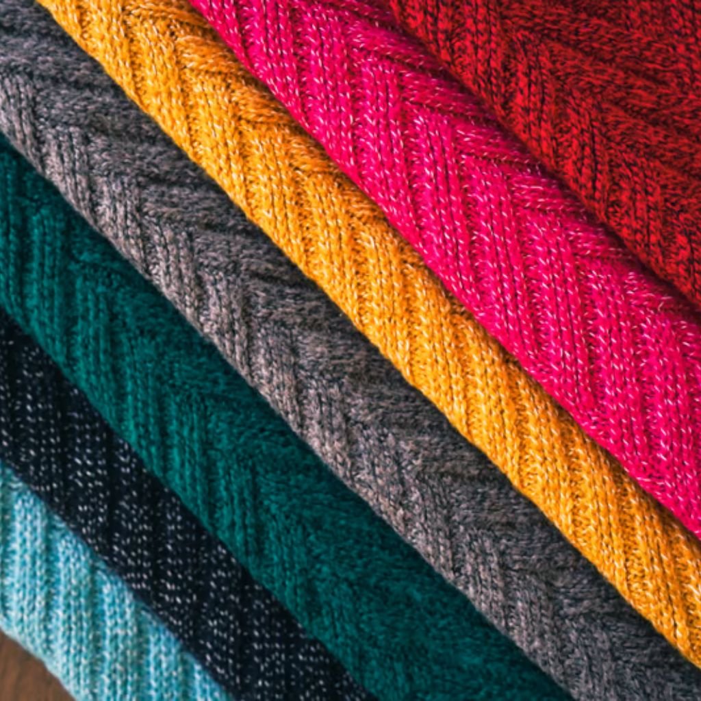 Alt text: Close-up of a stack of colorful knitted fabrics in diagonal rows, showing textures and patterns in teal, gray, yellow, pink, and red.
Winter Lock Fabric: