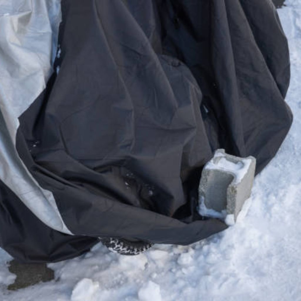 Alt text: A black and silver tarp-like cover lies on snow, weighed down by a grey concrete block with some snow on it.

Ice Barrier Windproof Fabric: