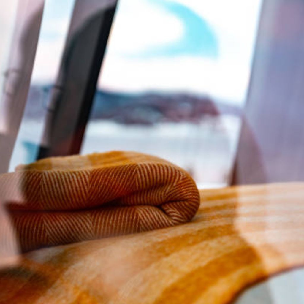 Alt text: Close-up of a folded yellow and brown patterned blanket with a window and snowy landscape visible in the blurred background.
Arctic Hug Comfort Weave:

