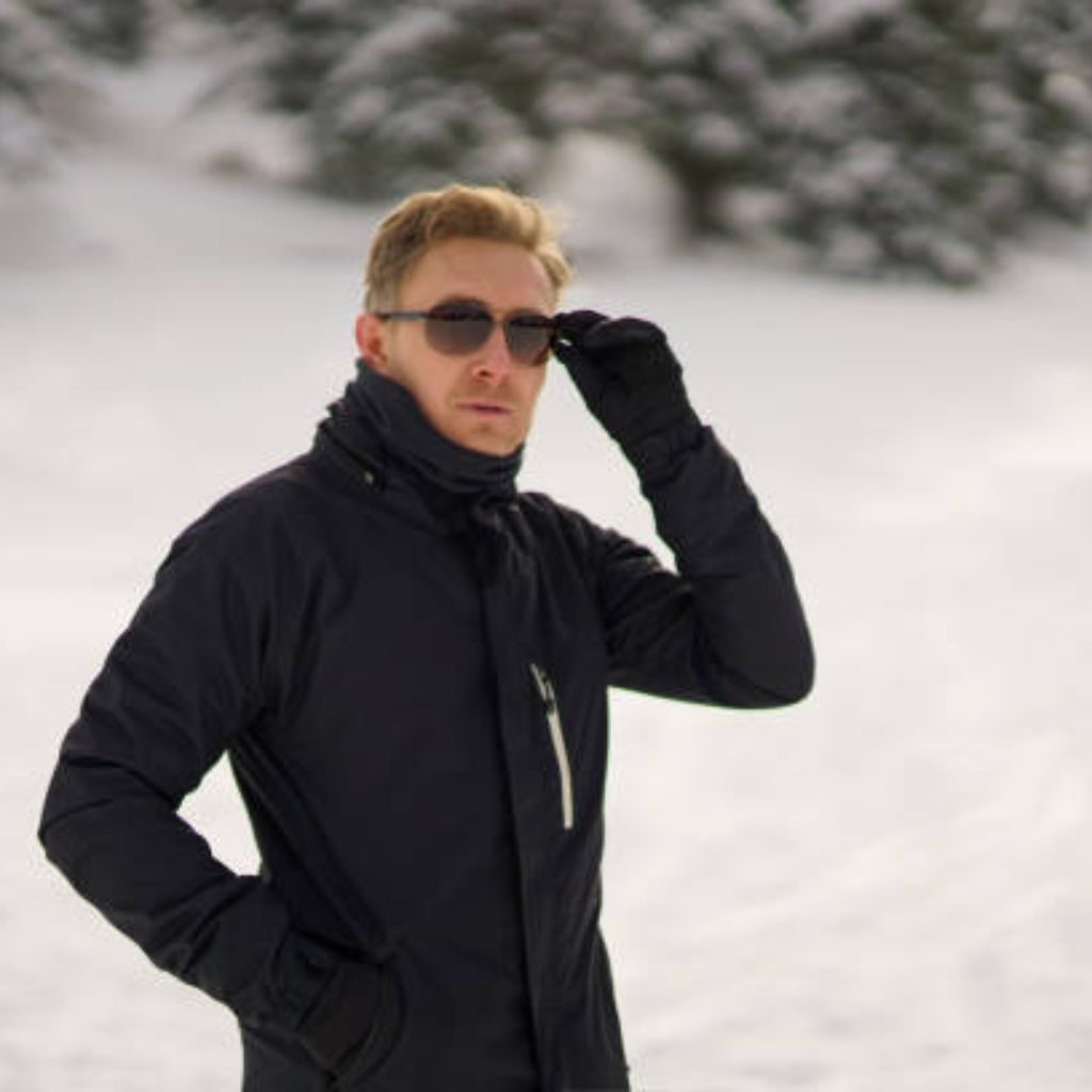 What Is Snow Barrier Climate Fabric? Features & Uses Details 8 Alt text: A man in a black winter jacket and gloves stands in a snowy landscape, adjusting his sunglasses with his right hand. He has blonde hair, and snow-covered trees are in the background.
What Is Snow Barrier Climate Fabric?