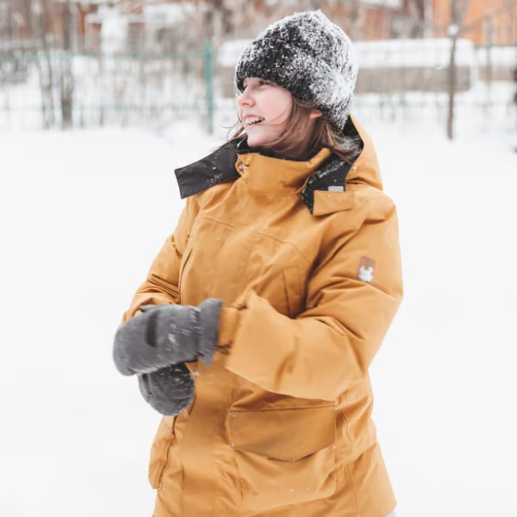 A smiling person outdoors in a snowy scene, wearing a mustard-brown military-inspired winter jacket with a high collar, gray gloves, a dark knit beanie, and snow on the hood.
Maximum Warmth Winter Coat: