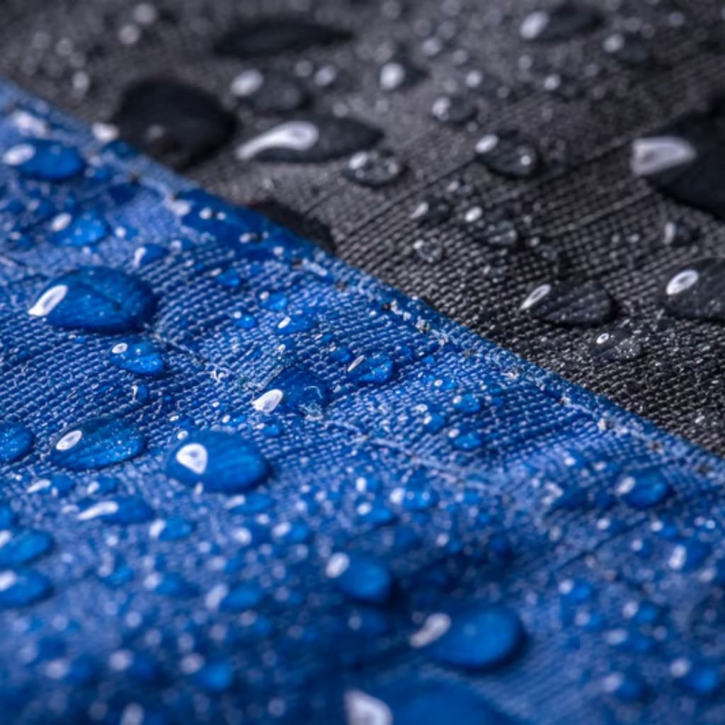 Close-up of blue and black waterproof fabric with scattered water droplets, highlighting the textured material and moisture resistance. How Gore-Tex Fabric Works: