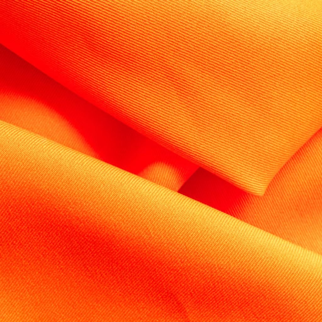 Close-up of textured orange fabric draped in soft folds, with visible weave and subtle light/shadow variations.

Softshell Fabric Explained: