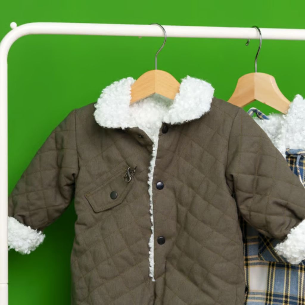Sherpa Lined Fabric Guide: Features, Advantages & Best Uses 10 Two children’s jackets hanging on a white rack against a bright green background: a quilted olive-green jacket with a white fuzzy collar and cuffs, and a blue-and-yellow plaid garment with a matching white fuzzy collar.
Sherpa Lined Fabric Guide: