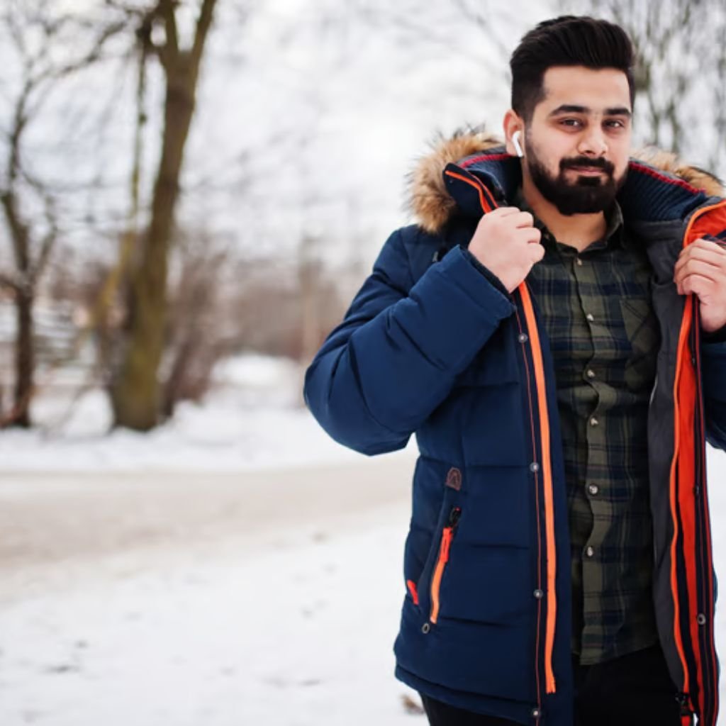 Heavyweight Insulated Winter Coat Explained: Features & Uses 9 A man outdoors in a snowy park wearing a navy blue winter jacket with a fur-lined hood, adjusting his coat while looking at the camera.Heavyweight Insulated Winter Coat Explained:
