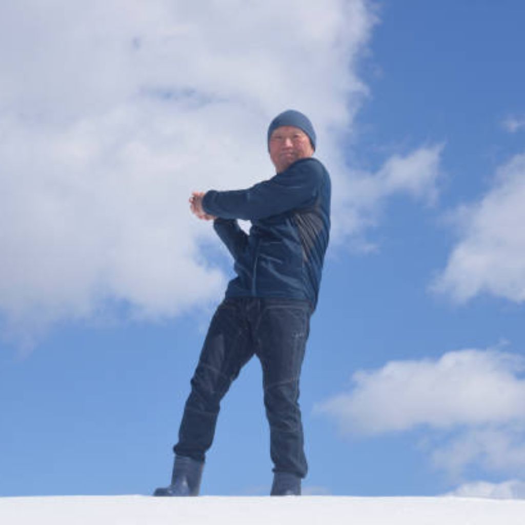 What Is Snow Barrier Climate Fabric? Features & Uses Details 10 Alt text: A man dressed in a dark blue winter outfit stands on a snowy surface, throwing a snowball against a bright blue sky with scattered white clouds.What Is Snow Barrier Climate Fabric?