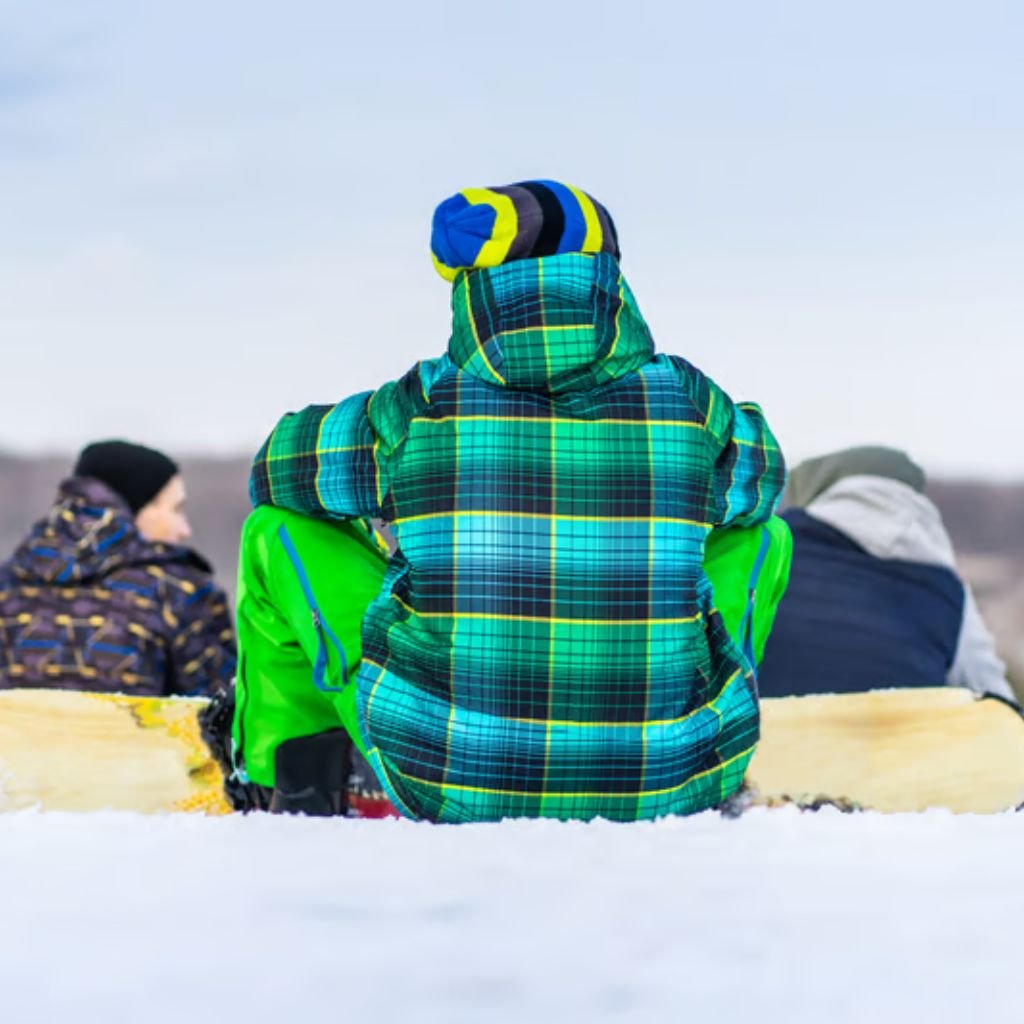 Alt text: A group of people sitting outdoors in a snowy landscape, wearing bright, plaid winter jackets. The central figure has a blue and green plaid jacket with a matching hat, facing away from the camera.

Arctic Shield Fabric: