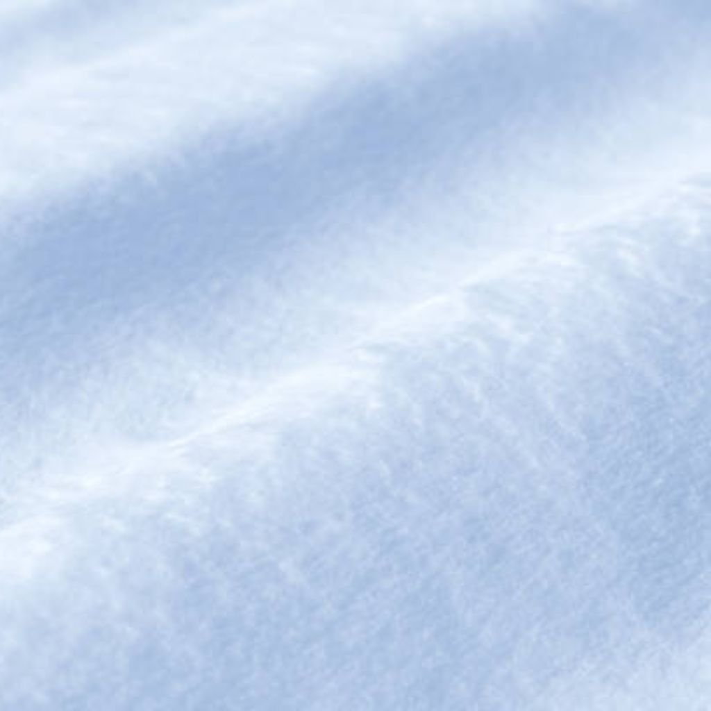 Alt text: A close-up view of snow with wavy, uneven texture, showing white and light blue shadows as if lit by the sky. The perspective is angled, with a vast field of snow extending into the distance.Snow Silk Luxe Winter Weave:
