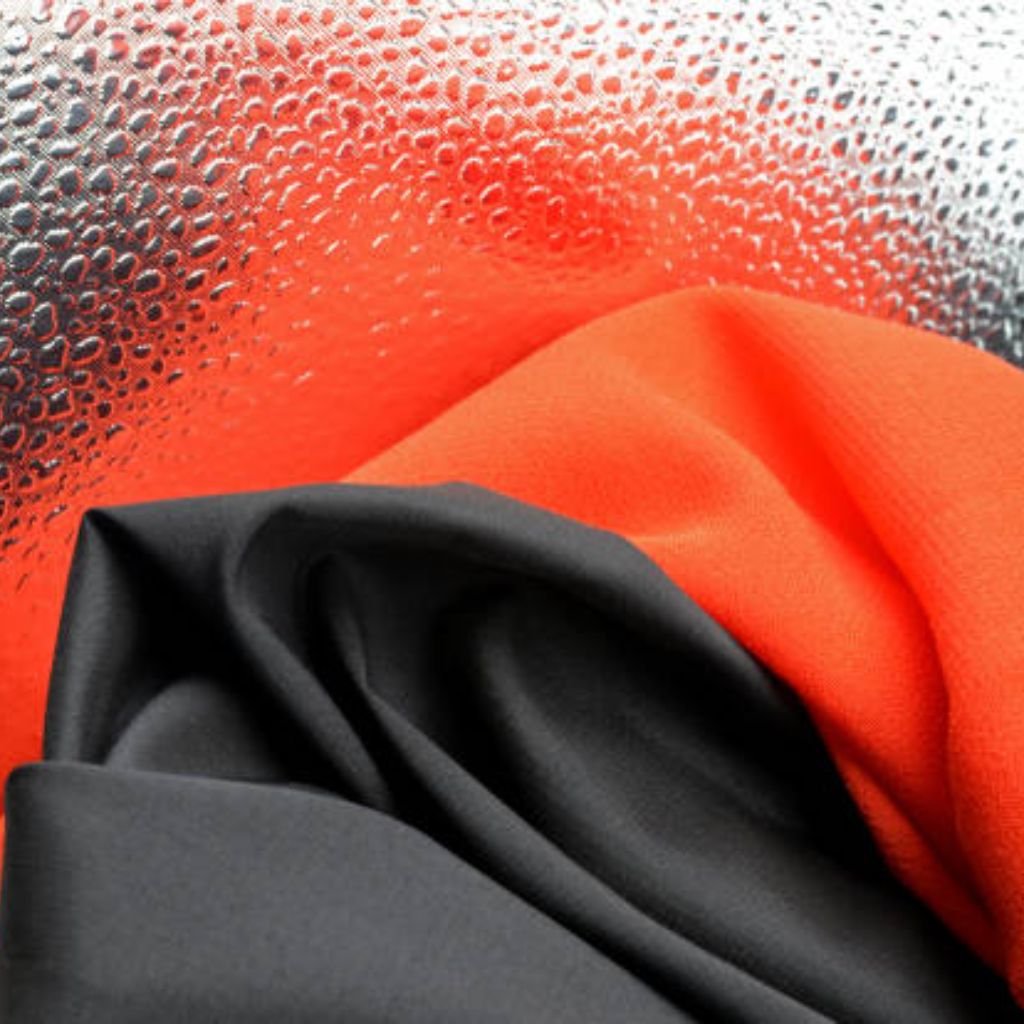 Polar Guard Heat Retention Fabric: Comfort Meets Performance 12 Alt text: Close-up image showing a silver, bumpy textured background with layered orange and dark grey fabrics draped over it, creating a rich, overlapping fold pattern.
Polar Guard Heat Retention Fabric: