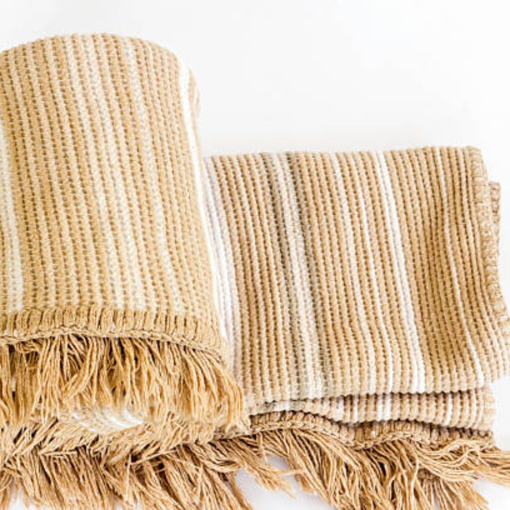 Alt text: A close-up of a tan and white striped woven blanket with a textured surface and fringed edges. The blanket is partially rolled on the left and laid flat on the right.
Arctic Hug Comfort Weave:

