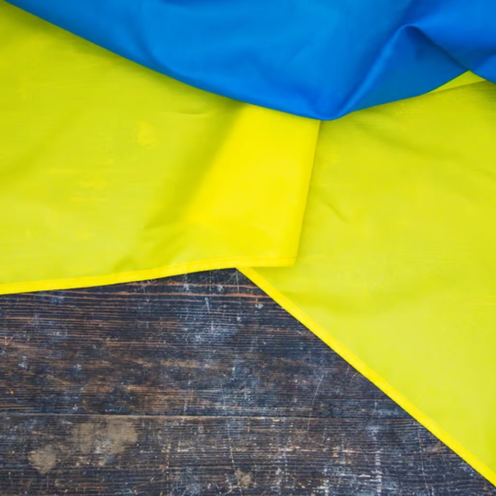 A close-up of the Ukrainian flag draped over a dark, weathered wooden surface. The blue stripe is at the top, with the yellow stripe in the middle and bottom, showing rough textures and scratches on the wood.
Softshell Fabric Explained:
