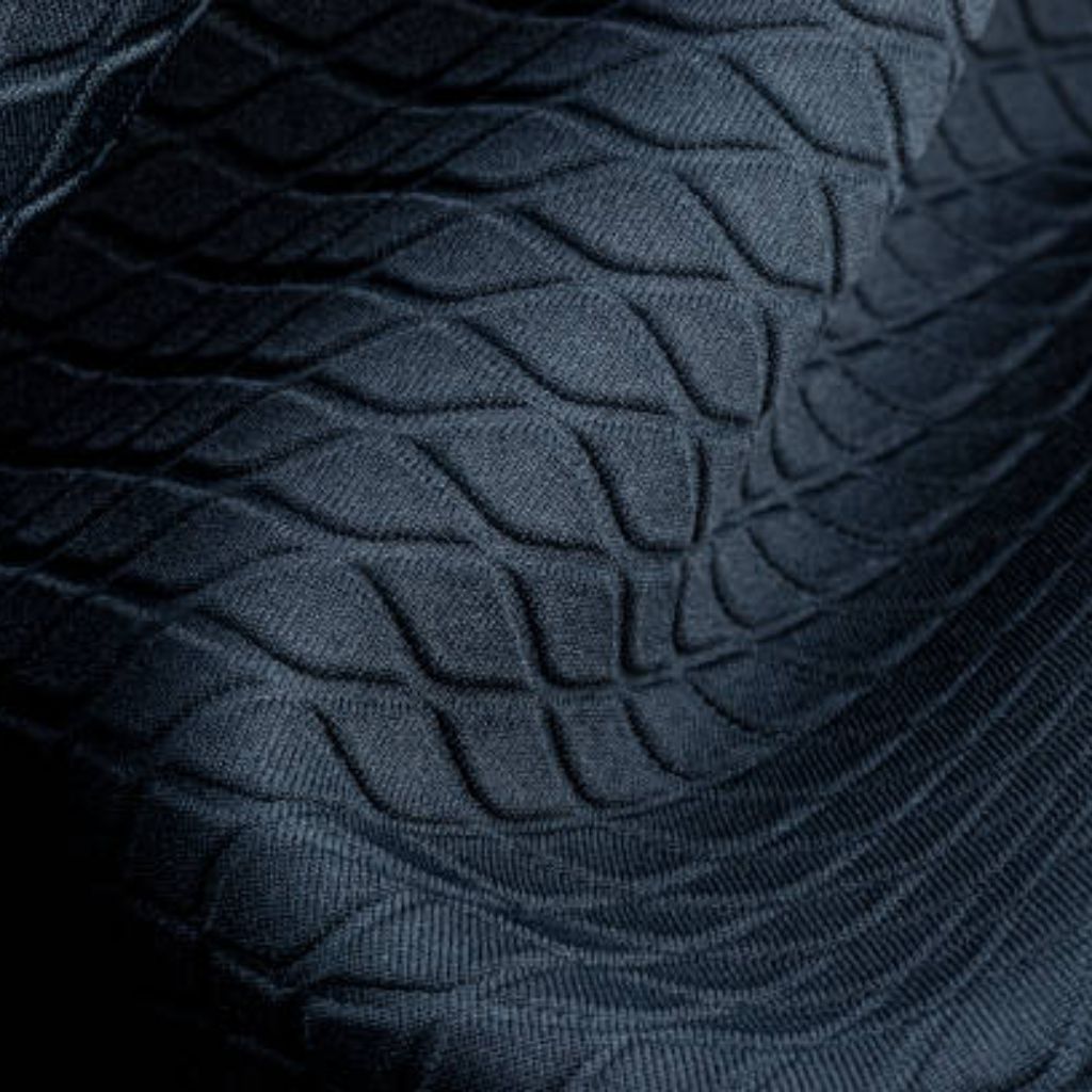 WarmTech Elite Athletic Weave: Next-Gen Athletic Fabric Tech 10 Alt text: Close-up of dark blue textured fabric with a repeating grid pattern of curved leaf-like shapes; light and shadow emphasize depth.
WarmTech Elite Athletic Weave:
