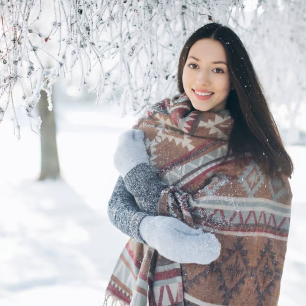 Alt text: A smiling young woman standing in a snowy landscape, wearing a grey sweater, light grey mittens, and a large patterned scarf.
Winter Lock Fabric:
