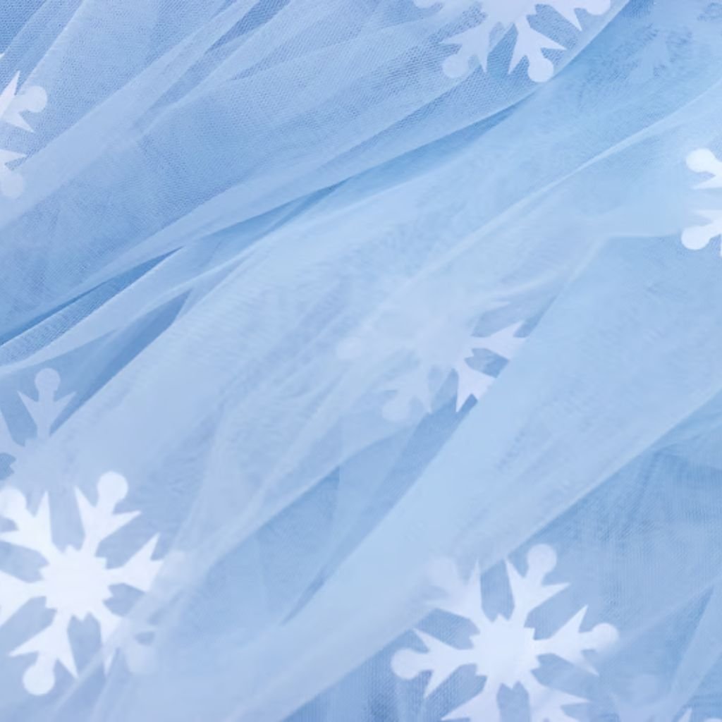 Alt text: A close-up view of light blue tulle fabric with white snowflake patterns scattered across the surface; the fabric is draped and folded, creating layered shadows and depth.
Frost Flex Fabric Explained: