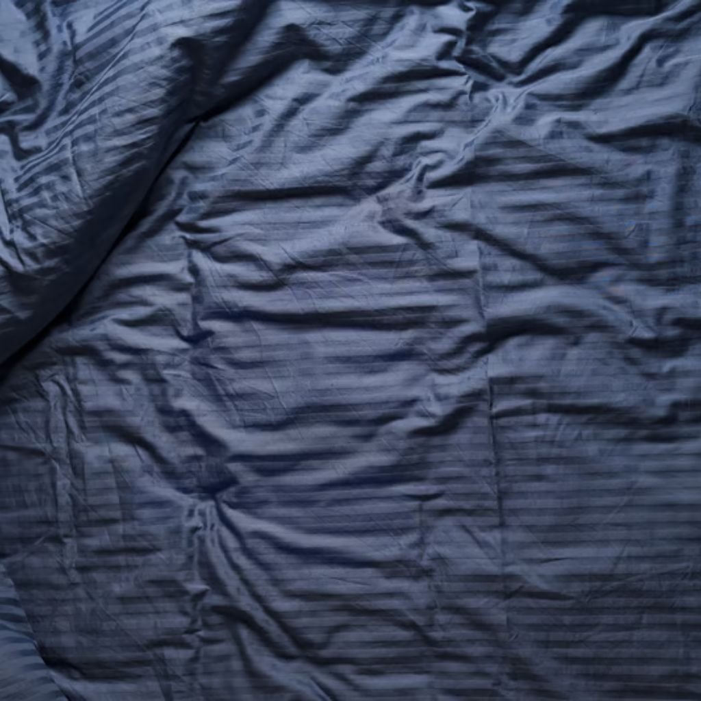 Storm Warm Insulation Fabric: Ultimate Winter Warmth Guide 6 Top-down view of a wrinkled blue striped bedsheet with horizontal lighter and darker blue stripes and soft shadows.
Storm Warm Insulation Fabric:
