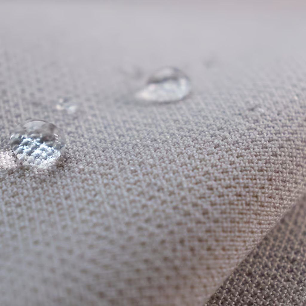 Alt text: Close-up of light beige woven fabric with three water droplets; the largest droplet magnifies the fabric, while two smaller droplets are above and in the background. The fabric texture forms a grid-like pattern.

Ice Barrier Windproof Fabric: