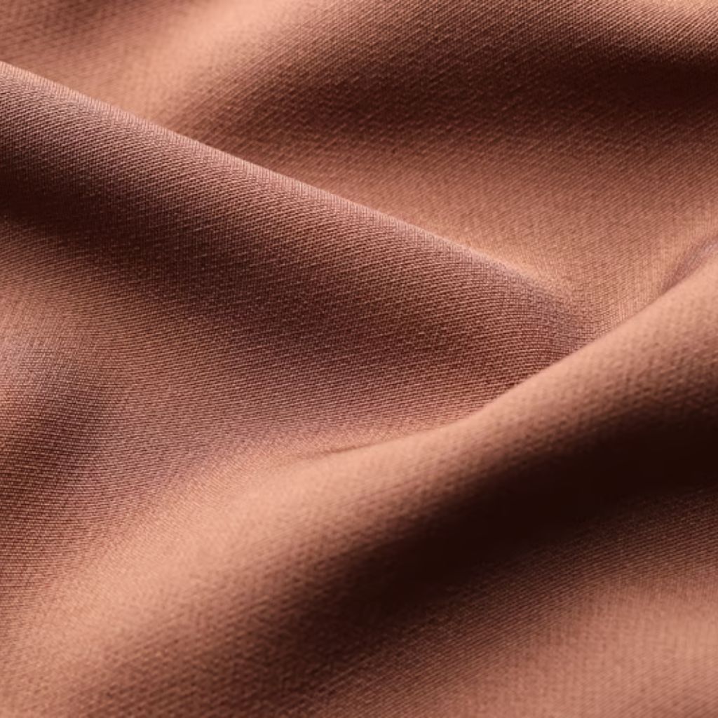 Warm Aura Fabric Explained:Why It’s Perfect for Cold Weather 6 Alt text: Close-up of a folded piece of solid reddish-brown fabric with a fine visible weave; folds create highlights and shadows that emphasize the fabric’s texture.
Warm Aura Fabric Explained: