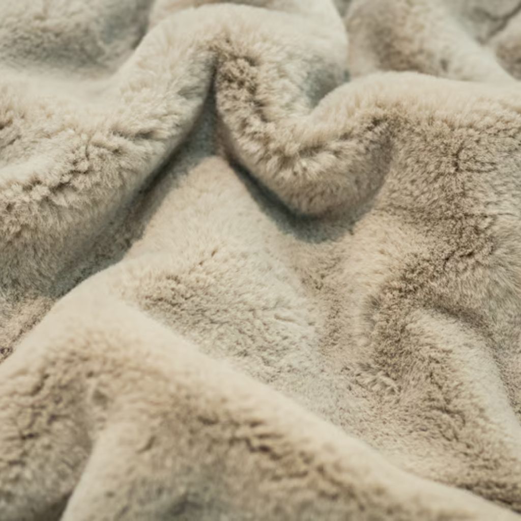 Close-up of light brown faux fur fabric with soft, plush texture. The material is creased and folded, creating shadows and highlights.Nordic Plush Thermal Fabric Explained:
