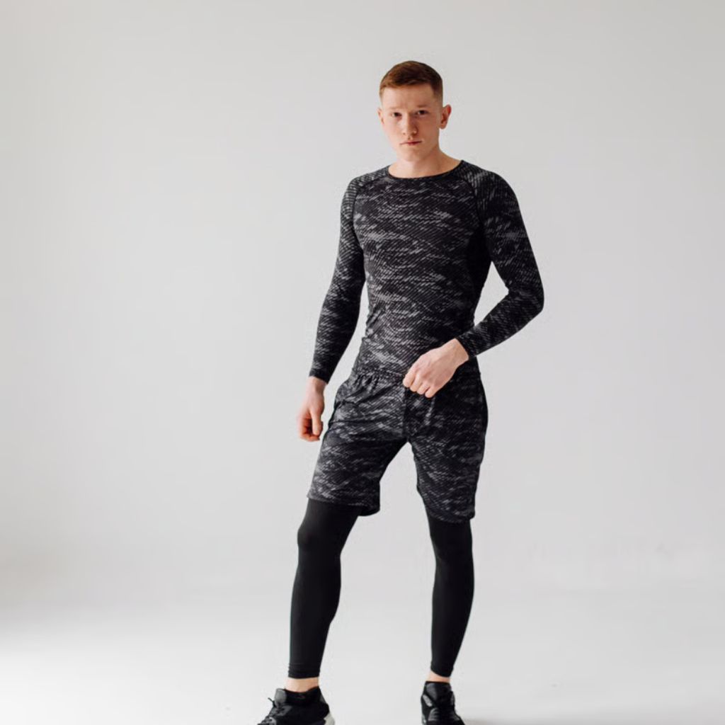 A full-body shot of a fair-skinned man with red hair standing in a studio with a white background. He wears a gray patterned long-sleeve shirt, matching patterned shorts, black leggings, and black sneakers. His right hand is in his pocket as he looks at the camera.
Power Dry Elite Knit Technology: