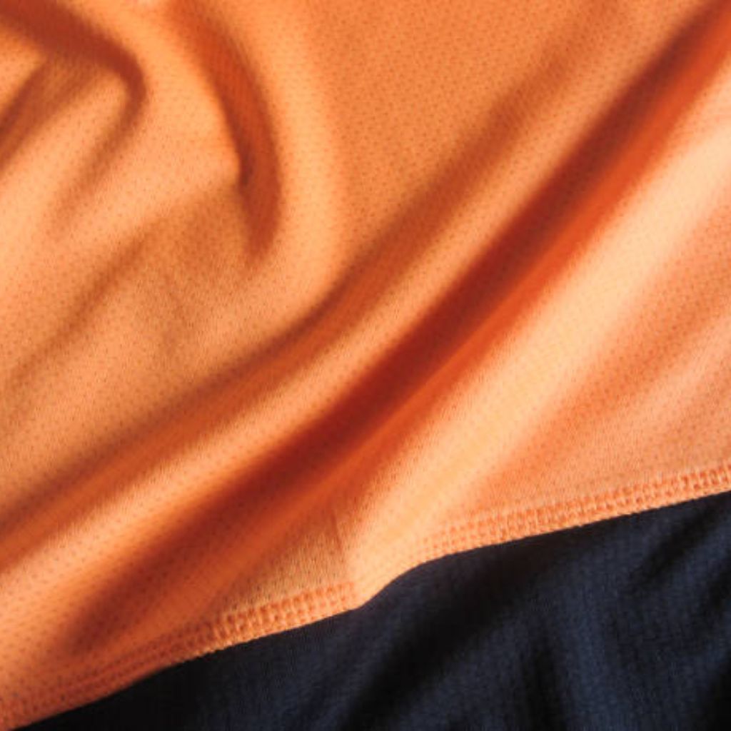 Close-up of two fabrics: bright orange breathable material with a perforated texture meeting a dark navy blue fabric at a seam edge.
Heat Core Insulated Sports Textile: