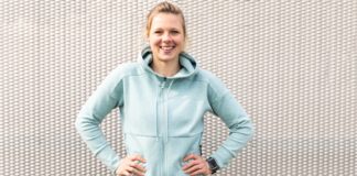 Performance Zip Hoodie: Ultimate Comfort & Style Smiling woman standing with hands on hips in front of a textured white wall, wearing a light blue zip hoodie and a smartwatch on her left wrist.