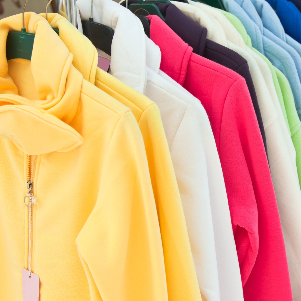 Classic Full-Zip Hoodie: Timeless Style & Everyday Comfort 4 A row of colorful zip-up hoodies hanging on a rack, with a bright yellow hoodie in the foreground and other colors including white, pink, purple, light green, and blue fading into the background.