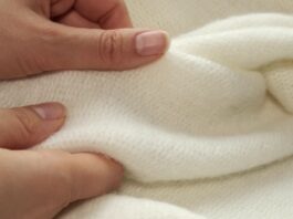 Recycled Cashmere Jersey Fabric Close-up of hands gently handling a soft cream-colored knit fabric with a plush, fuzzy surface.