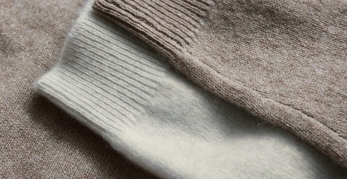 Recycled Grade C Cashmere Fabric A close-up view of a knitted garment showing two yarn colors: a light brown section with ribbed texture and an adjacent off-white section with smoother, more uniform knitting.