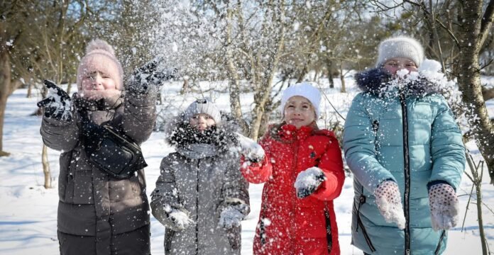 Alt text (short description): Four people in winter jackets are playing in the snow, throwing powdery snow into the air. Weather-Resistant Winter Coat: