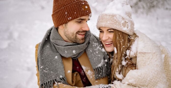 Alt text: A smiling couple bundled in winter clothing sits close together in a snowy outdoor setting, wearing knit hats, scarves, and thick coats. Cold Wind Blocking Winter Coat