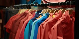 How Gore-Tex Fabric Works: The Science of Weather Protection A rack of colorful jackets hanging on wooden hangers in a store or closet, featuring shades of red, pink, blue, and teal. How Gore-Tex Fabric Works: