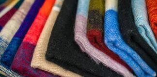 Sustainable Wool Fabric: Natural Warmth with a Green Promise Alt text: Close-up of a neatly stacked pile of folded fabrics in a diagonal arrangement. Colors include blue, red, orange, beige, black, purple, and green with some patterns; the texture appears soft and warm. Sustainable Wool Fabric: