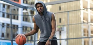 Sleeveless Hoodies: Style, Comfort, and Year Round Wear Now Athletic African-American man in a gray sleeveless hoodie dribbling a basketball on an outdoor court, wearing a watch. Buildings and a wire fence are in the background.