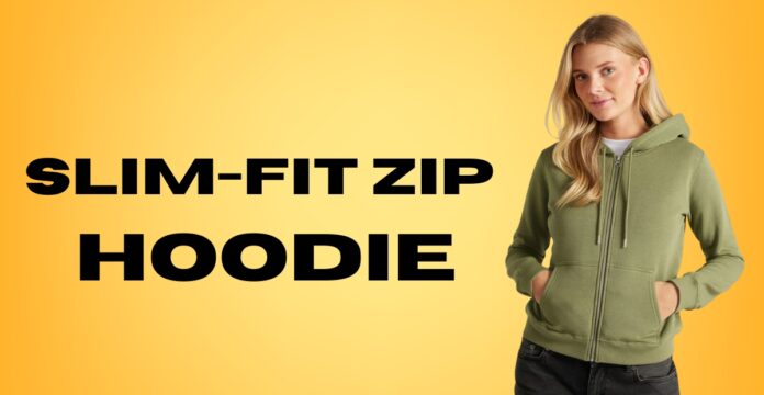 A woman with blond hair wearing a light olive-green slim-fit zip hoodie, standing against a bright yellow background. She has her hands in the pockets and is wearing dark jeans.