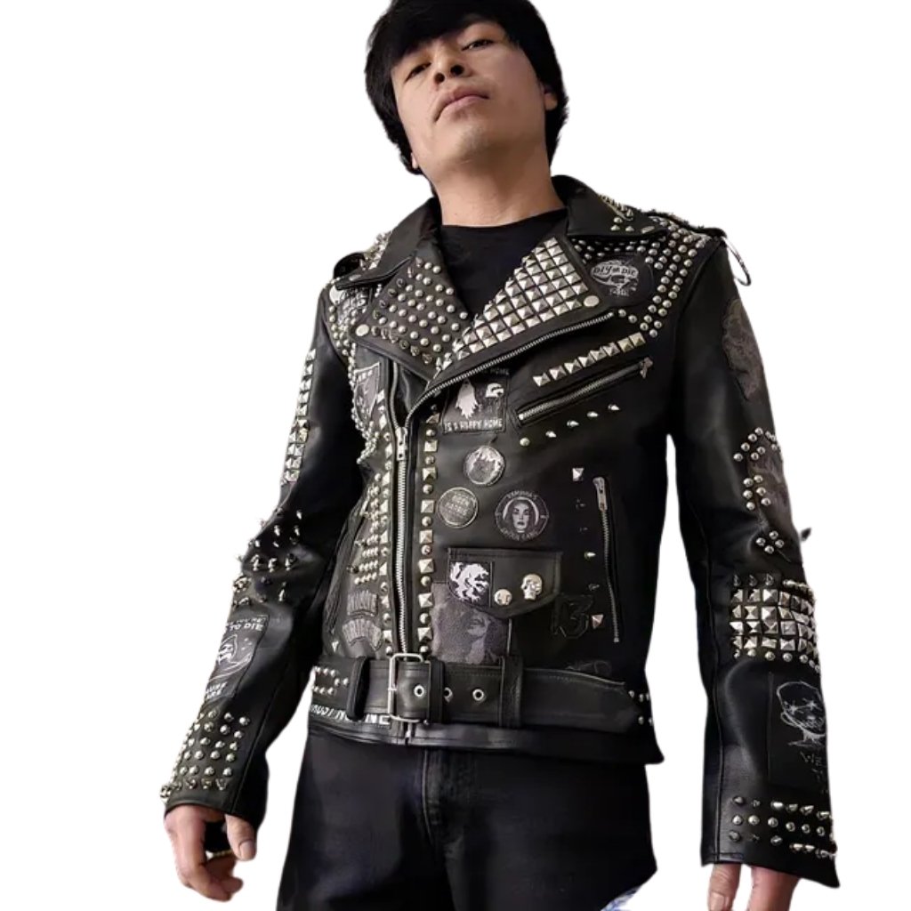 : A young man wearing a black studded leather jacket with numerous metal studs and patches, standing against a plain white background. He wears a black t-shirt and black pants, with a confident pose.