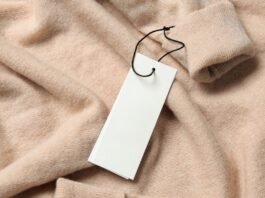 Sustainable Grade B Cashmere Close-up of a light peach cashmere sweater with a blank white tag hanging from a black string, casually folded to show a cuff in the upper right corner.