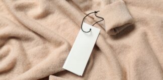 Sustainable Grade B Cashmere: Smart Luxury Choice Sustainable Grade B Cashmere Close-up of a light peach cashmere sweater with a blank white tag hanging from a black string, casually folded to show a cuff in the upper right corner.