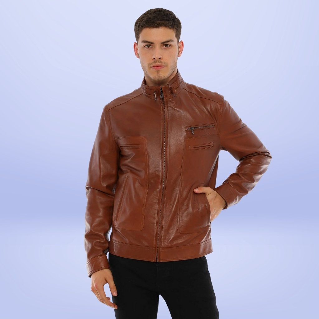 A man wearing a tan brown leather jacket stands against a light blue gradient backdrop, with one hand in his jacket pocket and looking at the camera.
