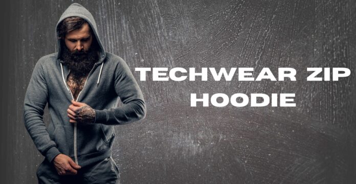 A bearded man in a gray zip-up hoodie stands against a textured gray background, partially zipping up the hoodie. Text on the right reads “TECHWEAR ZIP HOODIE.”