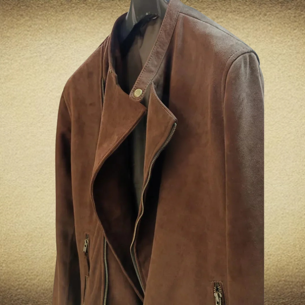 A brown nubuck leather jacket hangs on a black hanger against a textured beige background. The biker-style jacket features an asymmetrical zipper, a snap-fastened collar, and visible front zipper pockets.