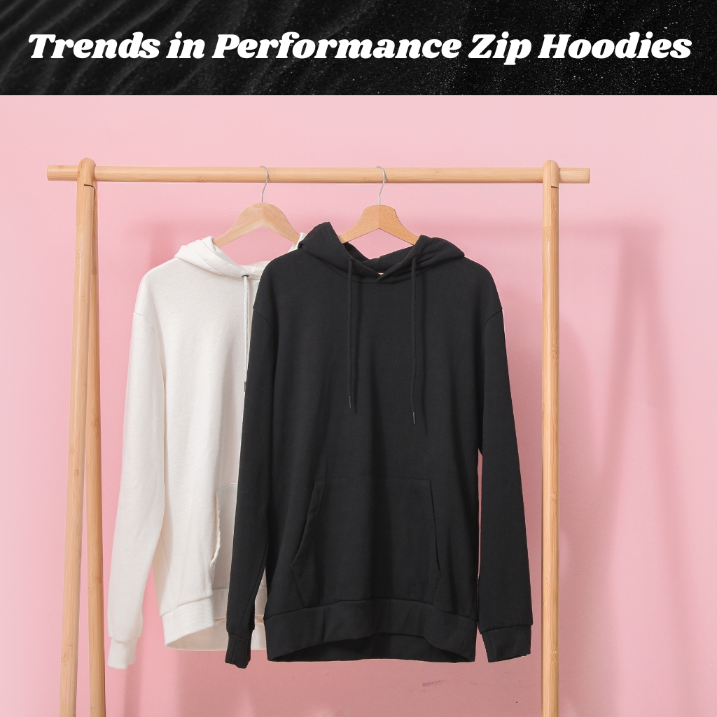 Two hoodies hang on a wooden rack against a light pink background: a white hoodie on the left and a black hoodie on the right, both on wooden hangers.
