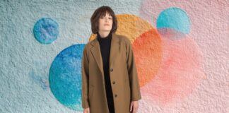 Types of Chesterfield Overcoat: Complete Style Guide Types of Chesterfield Overcoat A woman stands centered in a textured wall featuring abstract circular shapes in blue, orange, and pink. She wears a brown Chesterfield overcoat over a black turtleneck and has dark hair with bangs.