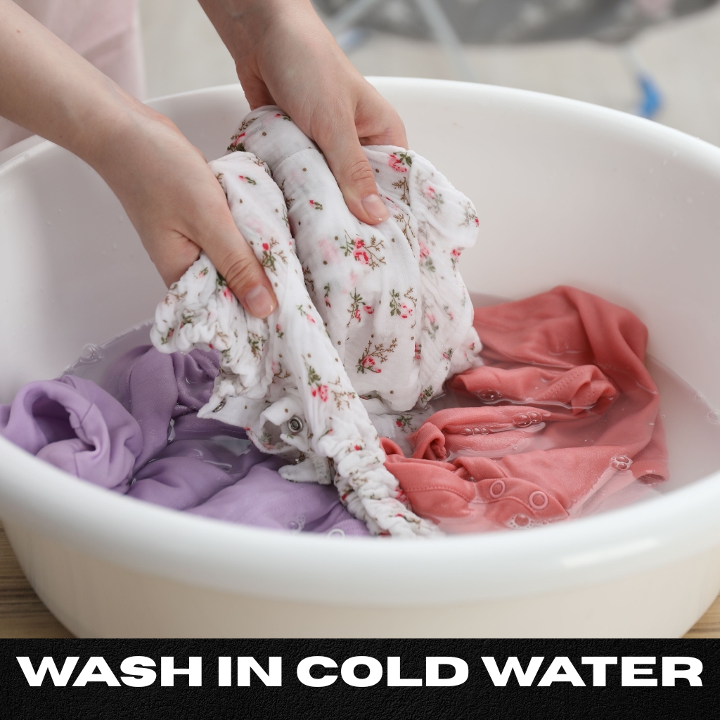 Hands wringing a white floral fabric in a white basin filled with water, with lavender and pink clothes submerged; text reads “WASH IN COLD WATER.” ripped zip hoodie
