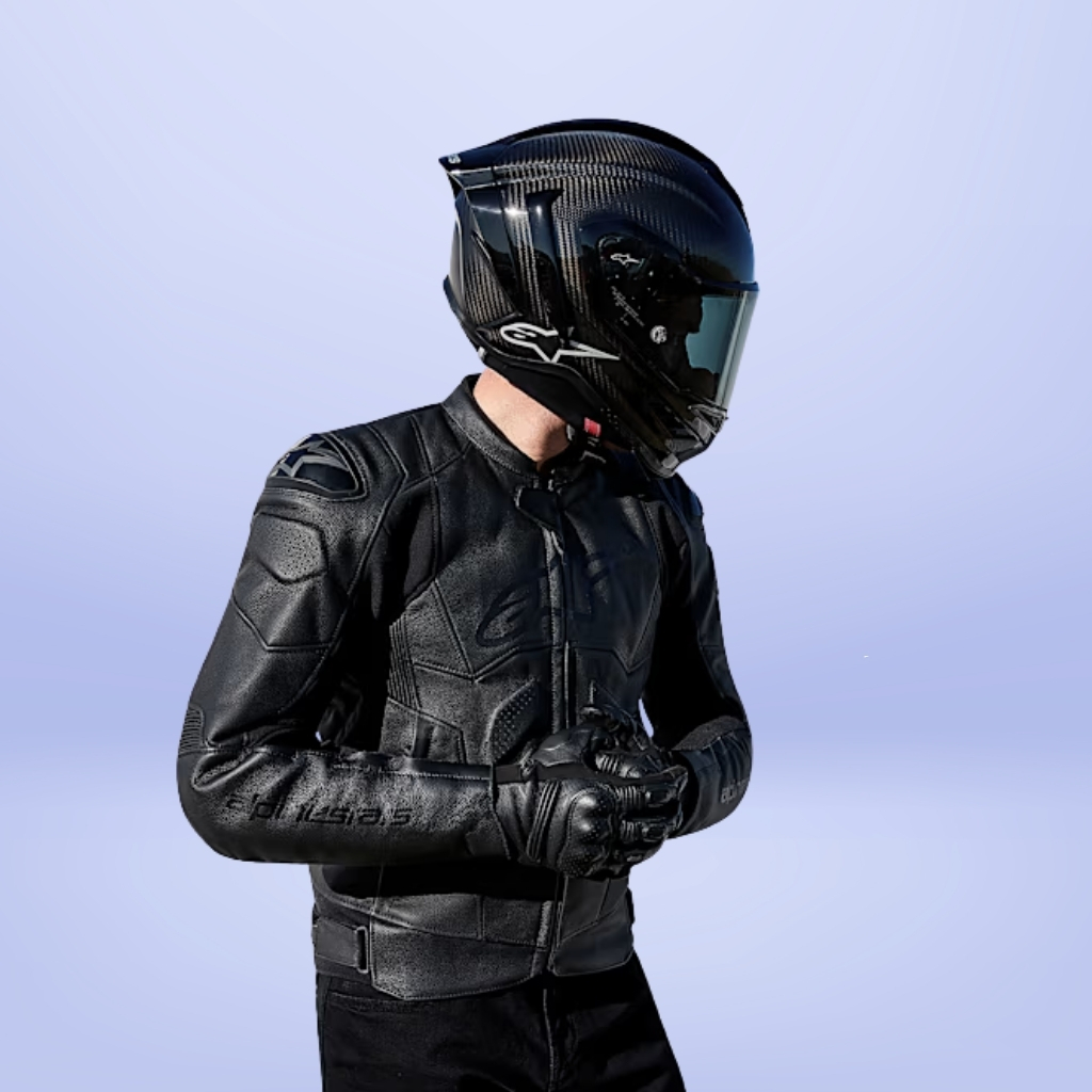 A person wearing a glossy black motorcycle helmet and a detailed black leather jacket stands with hands clasped in front. The pale blue background contrasts with the dark gear.