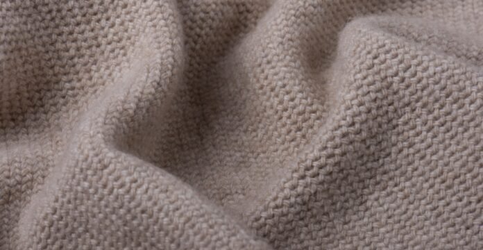Woven Grade C Cashmere Close-up of beige knitted fabric with a visible textured knit pattern and soft folds.