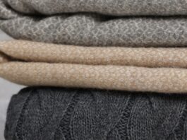 Woven Pure Cashmere Fabric Close-up of three folded knit blankets stacked in dark gray cable knit, light beige textured weave, and gray diamond-pattern knit, with a soft, cozy appearance and a blurred light gray background.