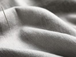 Woven Recycled Cashmere Fabric An acupuncture needle inserted into gray woven fabric, showing a thin silver needle with a textured handle amid softly draped folds.