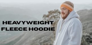 Heavyweight Fleece Hoodies: Ultimate Warmth & Comfort Guide A man with a beard wearing an orange-and-white striped beanie and a light-colored fleece hoodie stands outdoors on a misty mountain overlook.