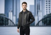 Stylish Nubuck Leather Jacket for Everyday Smart Looks A man standing outdoors in an urban setting, wearing a black nubuck leather jacket, a dark gray sweater, and black jeans. The cityscape in the background is blurred.