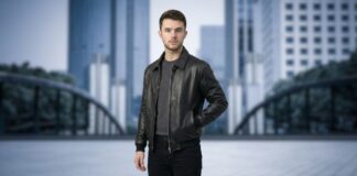 Stylish Nubuck Leather Jacket for Everyday Smart Looks A man standing outdoors in an urban setting, wearing a black nubuck leather jacket, a dark gray sweater, and black jeans. The cityscape in the background is blurred.